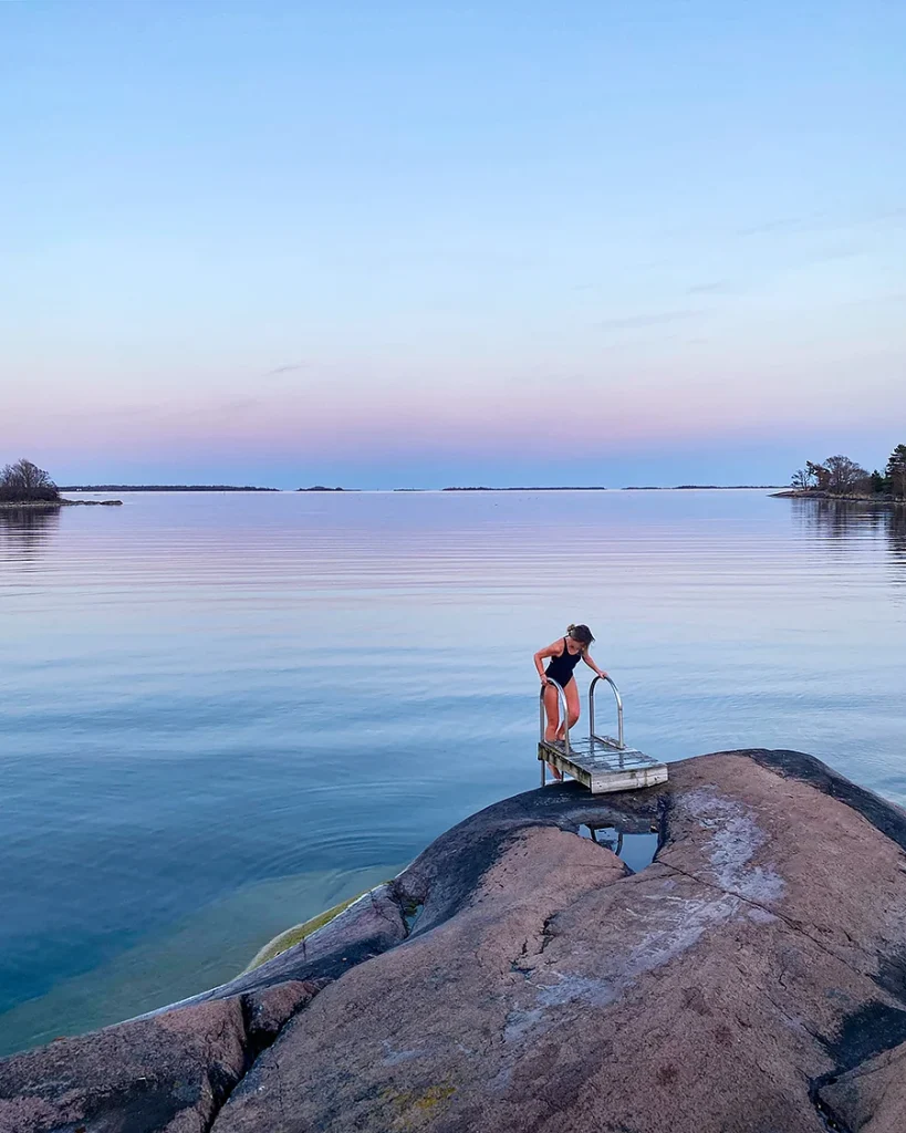 Kvinna vid badbrygga på Åland, redo för ett dopp. Vackert Åländskt landskap i bakgrunden.
